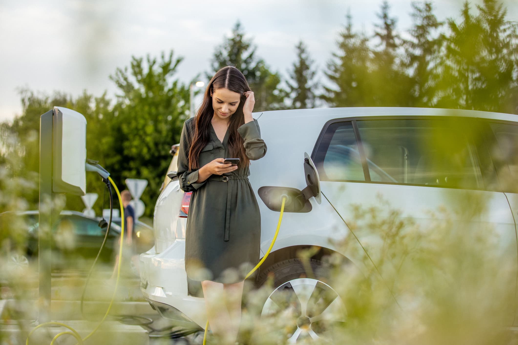 A woman checks her app while charging her EV