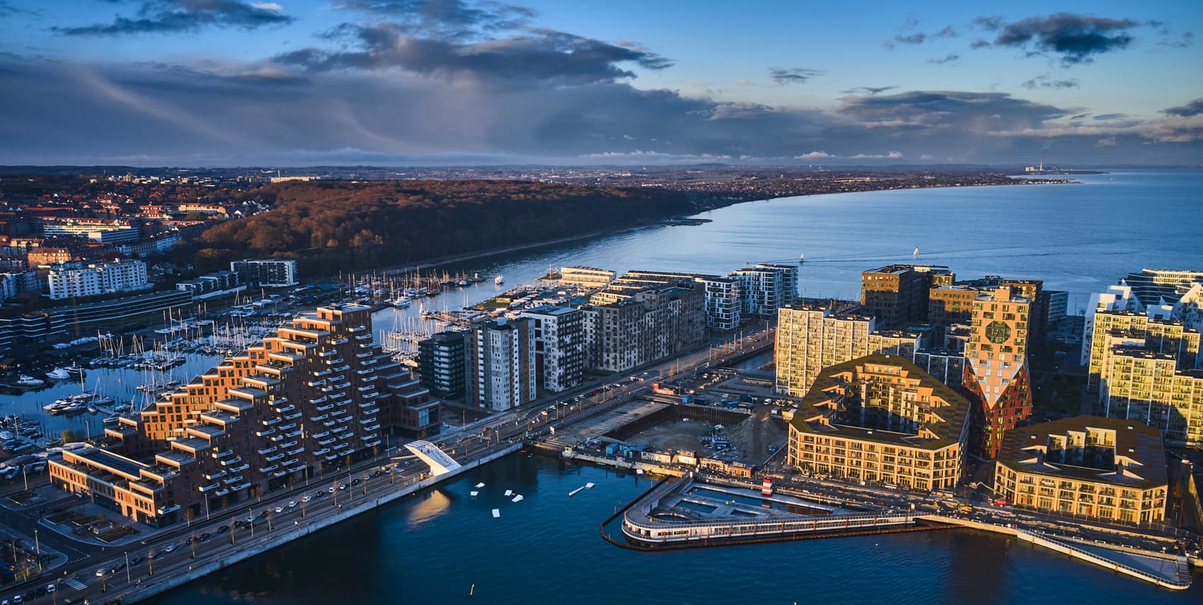 Aerial view of Aarhus waterfront with modern buildings, harbour, and coastline under a partly cloudy sky